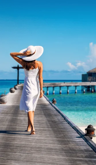 Woman in white dress walking on a tropical boardwalk – Fab Holidays, the best travel agency in Delhi.